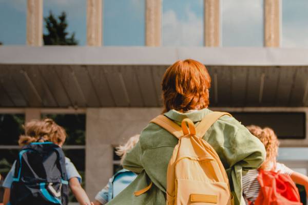 A group of children wearing backpacks, entering a school building