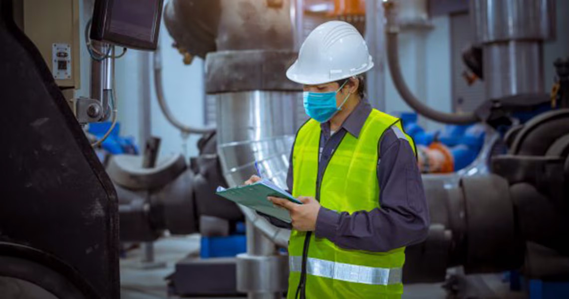 An engineer in protective gear reading a tablet in an industrial facility
