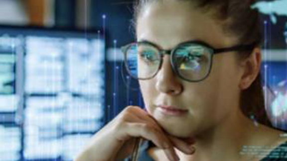 Close-up of a woman wearing glasses and looking at a monitor, with OpenBlue graphics in the background