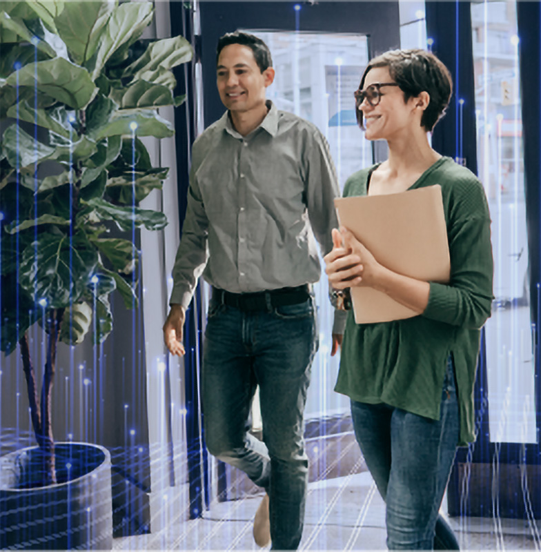A man and a woman smiling and entering an office, with plants near the door