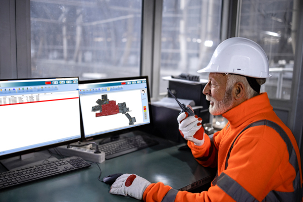 Man in safety gear working on two monitors and using a handheld transceiver